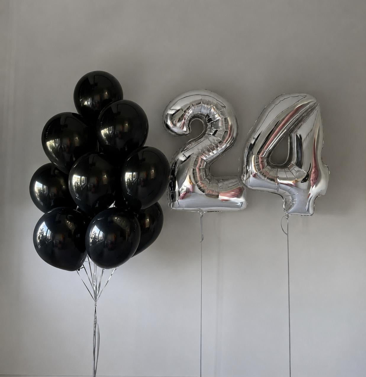 Black latex balloon bouquet with silver number 24 helium balloons on a neutral background.