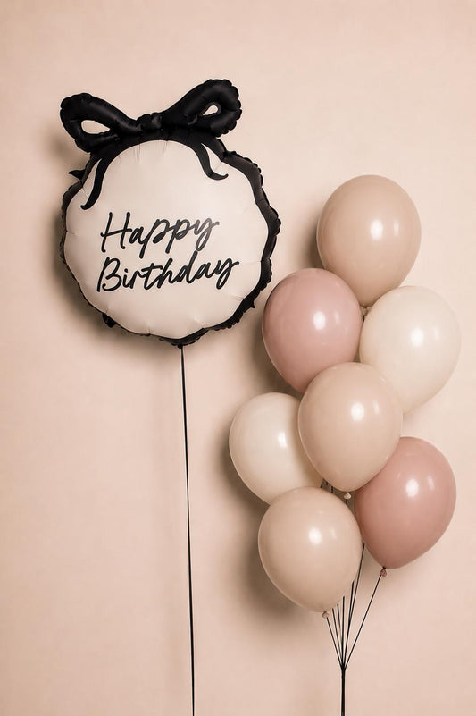 Elegant Happy Birthday foil balloon with black bow paired with blush, nude and ivory helium balloons in a minimal birthday bouquet arrangement.