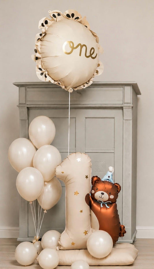 Neutral first birthday balloon arrangement featuring a personalised 'One' bubble balloon, number one foil balloon, teddy bear foil balloon and ivory helium balloons.