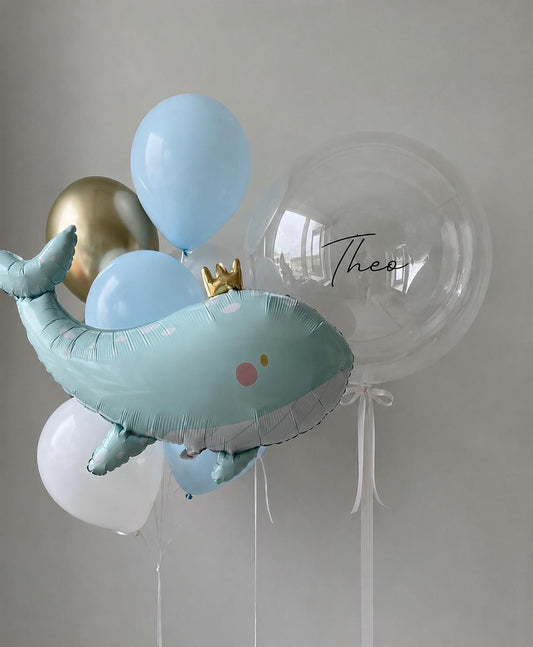 Personalised whale fish balloon bouquet with pastel blue, white and gold helium balloons on a neutral background.