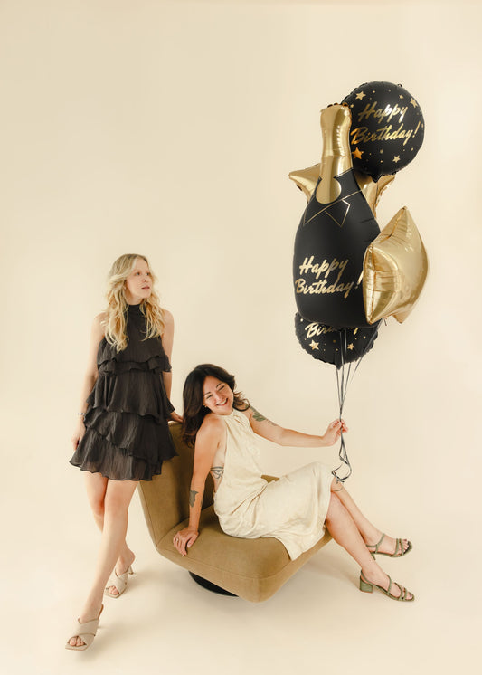 The Champagne Celebration Edit helium balloon bouquet featuring a black and gold champagne bottle foil balloon, two black Happy Birthday balloons and two champagne gold star balloons.