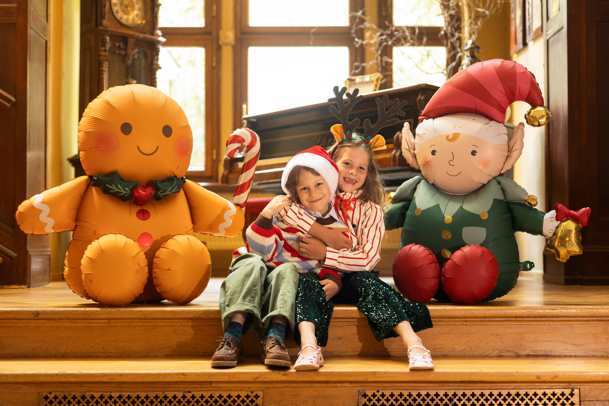The Christmas Characters Edit featuring a gingerbread man and Christmas elf foil balloon displayed in a festive Christmas setting with children.