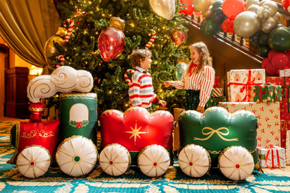 The Christmas Express Edit XXL Christmas train balloon displayed beside a decorated Christmas tree, featuring festive red and green carriages with elegant gold detailing.