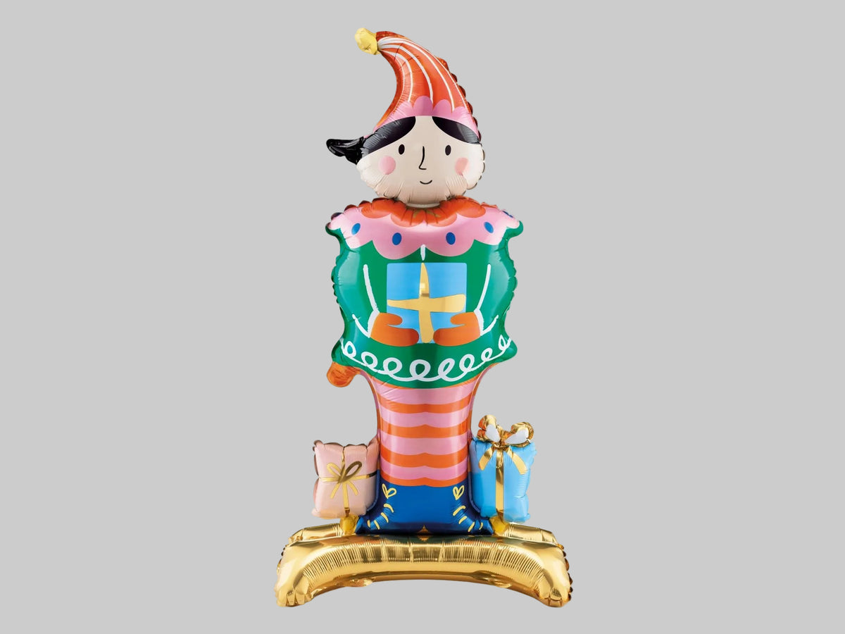 Colourful Christmas Nutcracker standing foil balloon featuring a tall striped hat, green jacket, pink and orange striped trousers and festive presents.