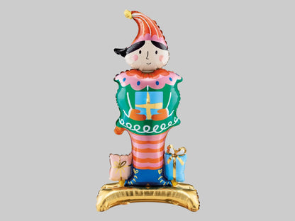 Colourful Christmas Nutcracker standing foil balloon featuring a tall striped hat, green jacket, pink and orange striped trousers and festive presents.
