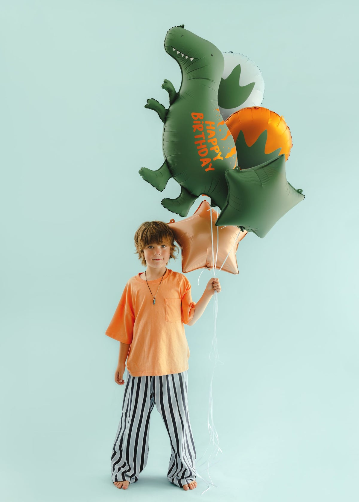 The Dino Roar Edit helium balloon bouquet featuring a green Happy Birthday dinosaur foil balloon, dinosaur footprint balloons and coordinating green and champagne gold stars.