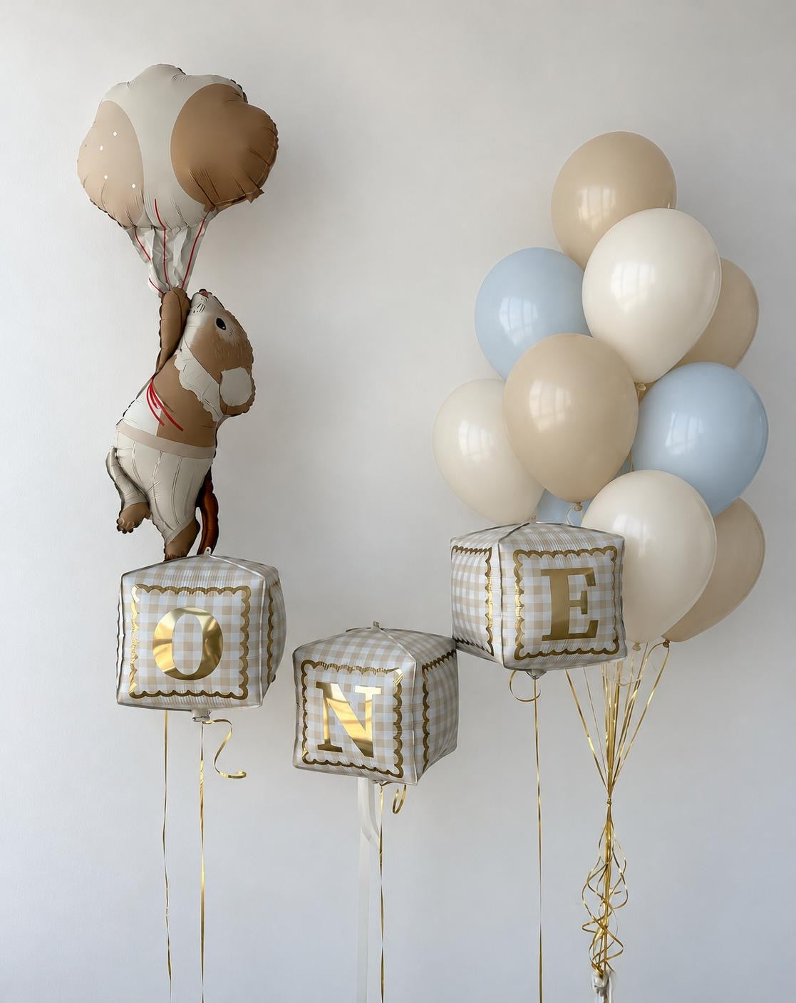The First Chapter Edit first birthday balloon arrangement featuring ONE letter cube balloons, a floating teddy bear and pastel blue, ivory and beige helium balloons.