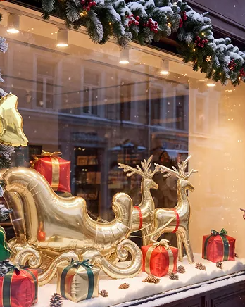 The Sleigh Edit Christmas balloon display featuring a metallic gold Santa sleigh, two gold reindeer foil balloons and six festive gift box balloons in red, green and gold.